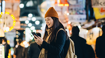 A young lady traveller looking at her mobile phone with a busy town background